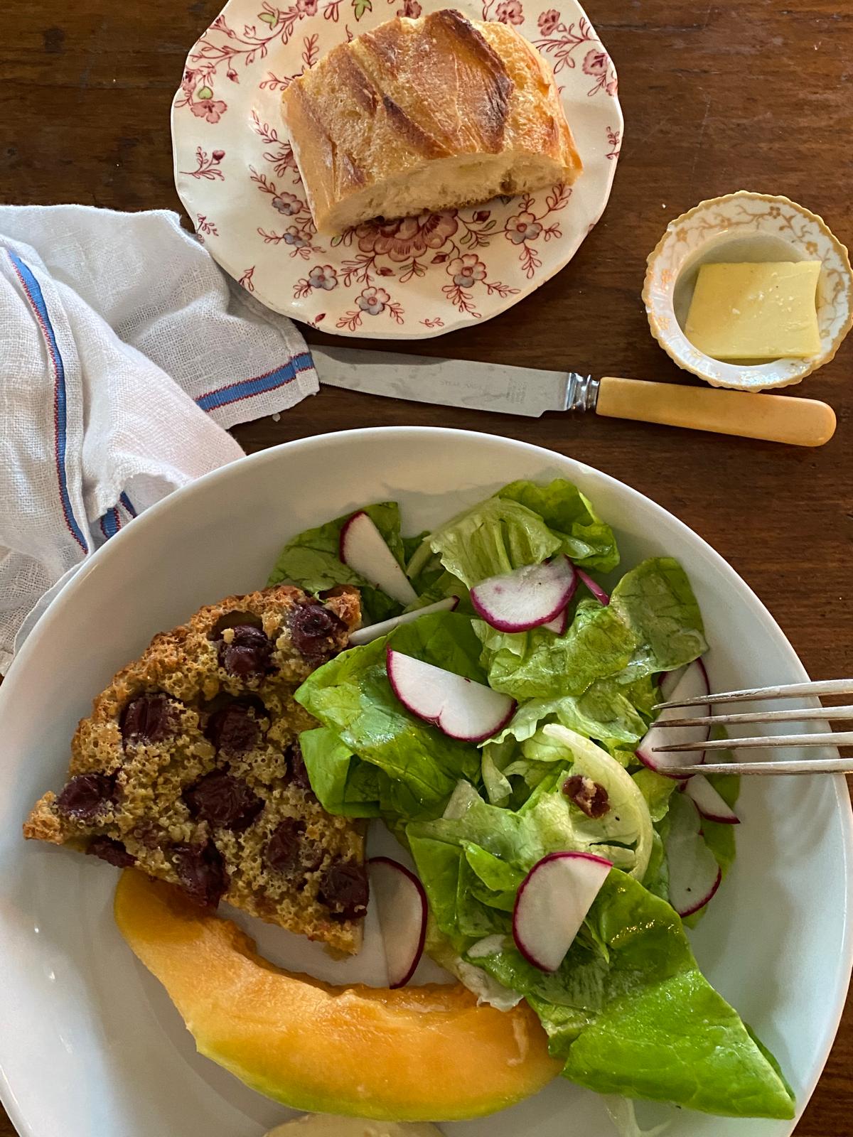 Garden salad with crisp radishes, seasonal fruit, and rustic seeded bread in a shallow bowl