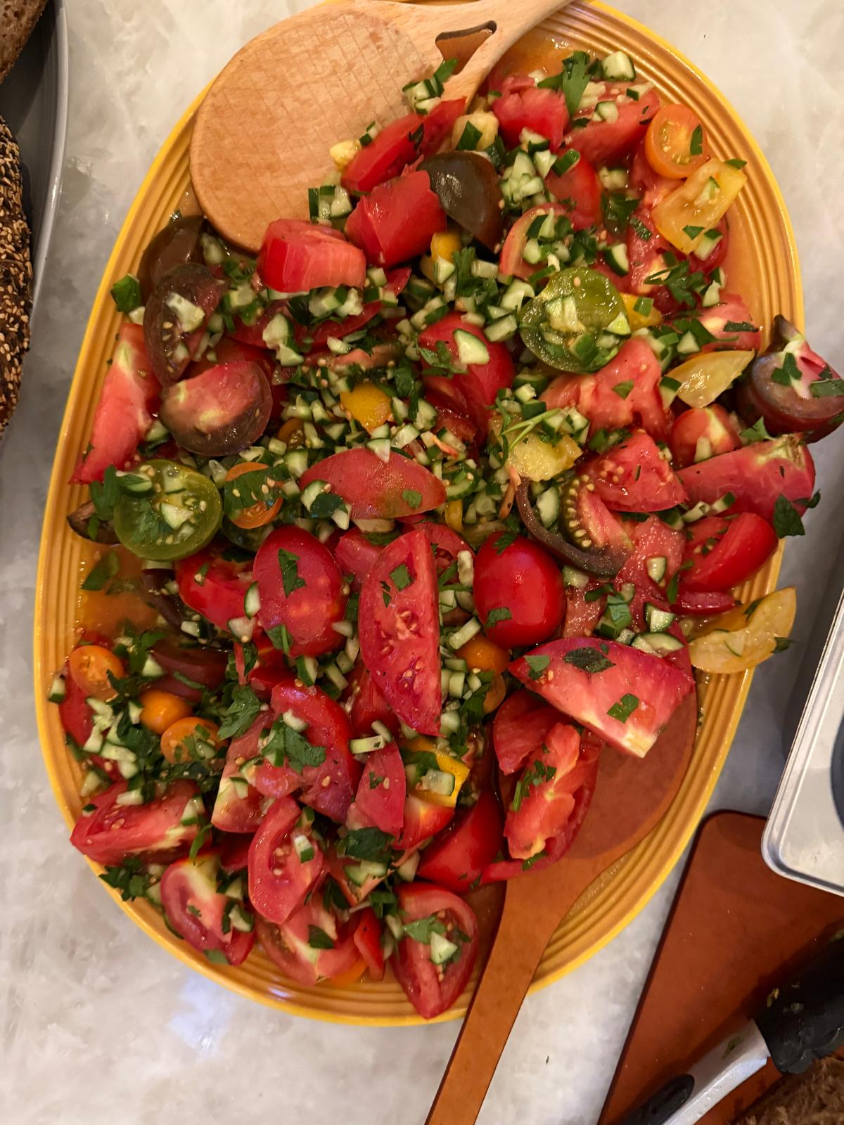Heirloom tomato salad with cucumber and herbs on a yellow platter
